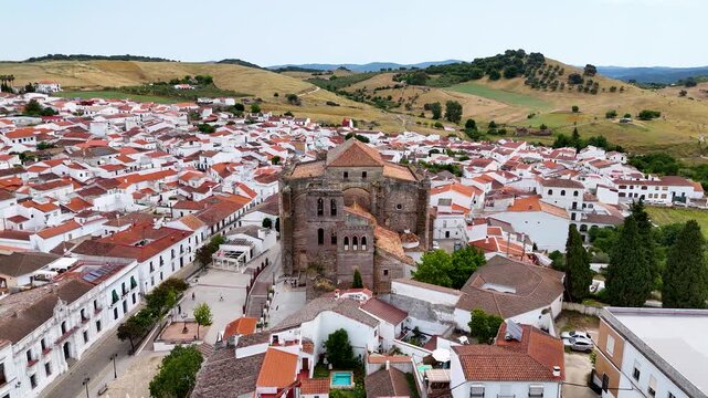 Aerial view of Iglesia de Nuestra Senora de la Consolacion surrounded by white houses and rolling hills in Cazalla de la Sierra, Andalucia, Spain.