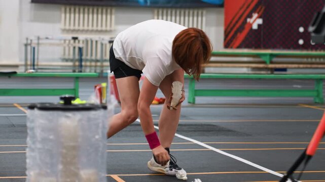 Solo shuttle collection. Competitive badminton athlete performing repeated pickups indoors. An athlete practices precise footwork by collecting shuttlecocks during focused indoor training