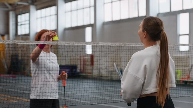 Indoor badminton coaching white coach instructing young player at net, friendly mentoring, sport drills, gymnasium light, close interaction, shuttlecock exchange, racket handoff, focused guidance,