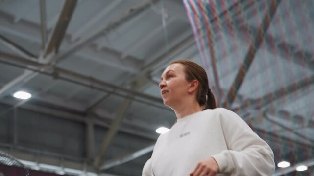 Caucasian woman indoor hall overhead drills focused young player practicing lobs and net control under high ceiling intense concentration racket control coach watching competitive preparation modern