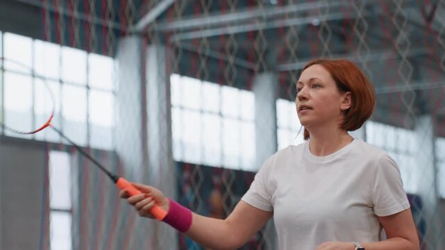 Indoor badminton court power serve with woman executing focused rally, fastpaced training drill, explosive smash attempts and sharp footwork, coachlike concentration, wristband flick and shirt damp