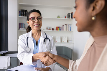 Cheerful middle aged physician shaking hands with young Black patient, giving respect, support, confidence, empathy. Healthy young African woman givin handshake to doctor, thanking for medical help © fizkes