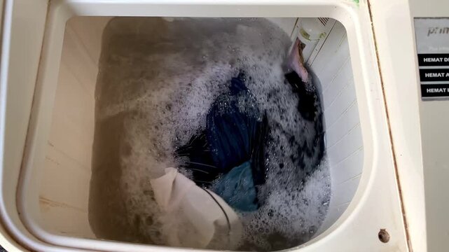 Clothes tumbling and swirling in a washing machine during the wash cycle.