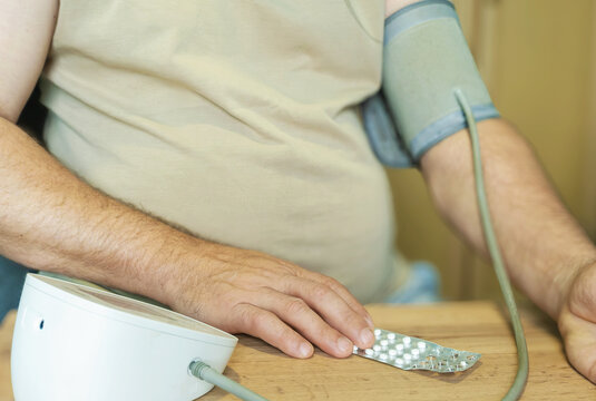 A person is using a digital blood pressure monitor, with the cuff wrapped around their upper arm and their hand holding the device.