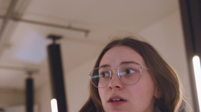 White woman close up surprised expression, young white tourist with glasses and brown coat reacting to sudden visual, eyebrows raised and mouth slightly open, soft LED backlight, interior corridor