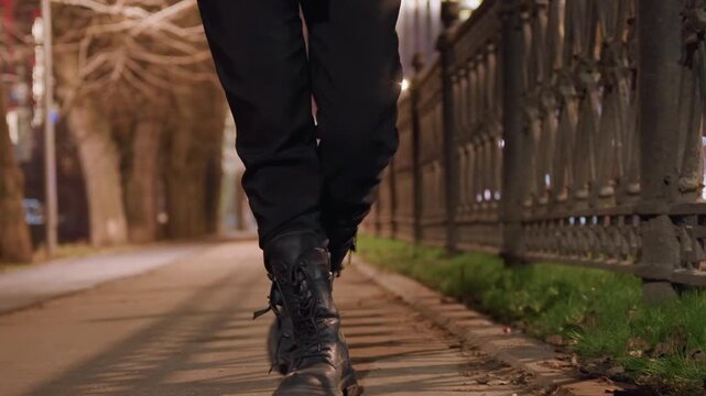 Night sidewalk boots brisk stride past iron fence, city lights bokeh and streetlight glow, confident commuter pace, cinematic street scene with reflective pavement and rhythmic footsteps.