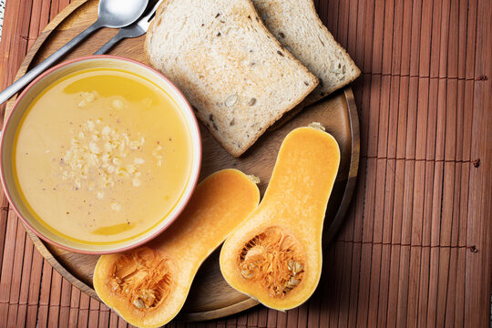 Creamy butternut squash soup with toasted whole grain bread and halved squash on wooden plate showing warm color texture blood circulation aids post surgical recovery