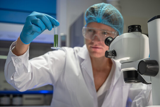 Focused male scientist wearing lab coat intently conducting research on epidemic strain using binocular microscope in  well equipped biomedical laboratory