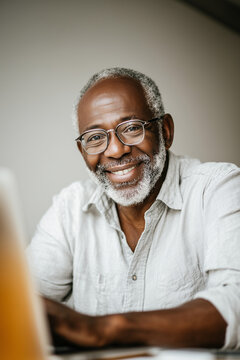 Senior confidently using digital technology at home, illustrating inclusion, independence, and modern connected living. Elderly man, dark skintone, using laptop, online banking, communication. Modern 