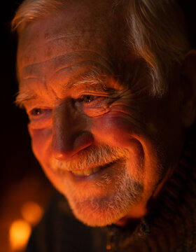 Smiling senior elderly man with beard looking away by warm orange firelight