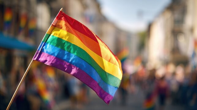 Rainbow flag waving at a vibrant LGBT parade, with a blurred crowd celebrating diversity in the background.