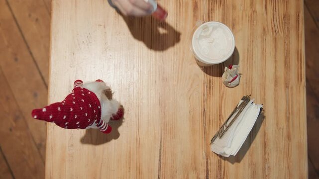Top view wooden table with gnome and hands laying note next to coffee, napkin holder and ornament cozy stationery moment, ribbon and tag, focused preparation for seasonal greeting