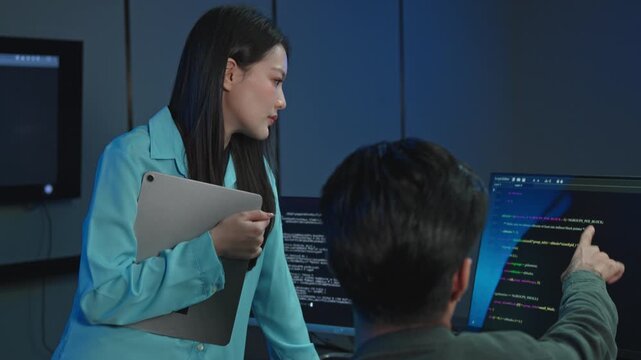 Professional Asian male and female software engineer team up to debug programming code, troubleshoot technical errors, and fix bugs on a computer monitor screen.