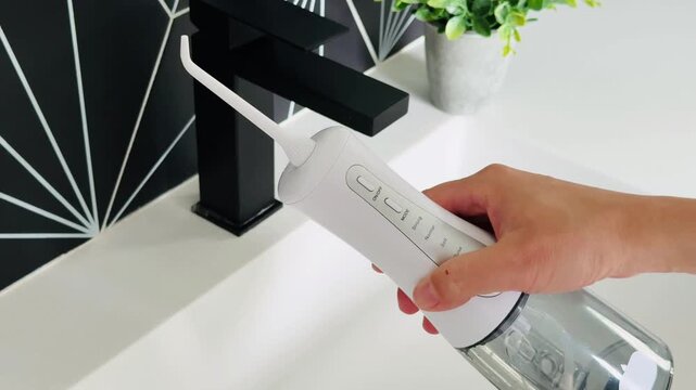 Oral flosser handle positioned above sink with sleek black faucet and modern geometric backdrop