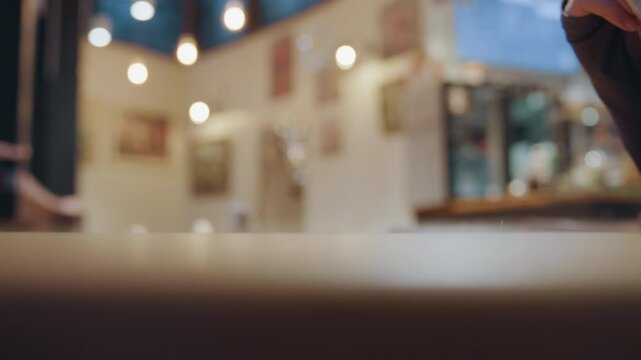 Wrapped treat held on table in bustling cafe, gloved hand lifts red ribbon bundle with slow deliberate motion, warm lights and wooden surface frame cinematic closeup full of tactile detail and evening
