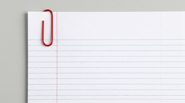 A single bright red metallic paper clip is securely attached to the top corner of a clean white sheet of lined notebook paper for organization.