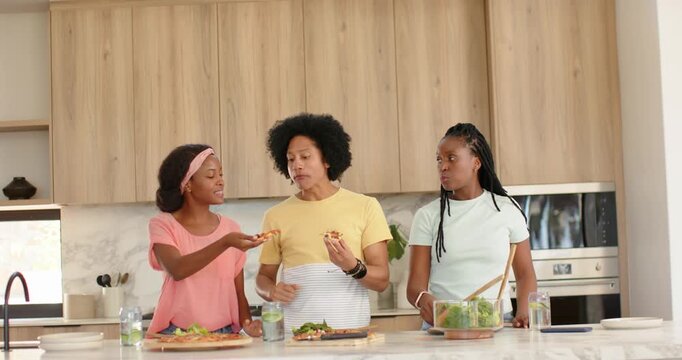 African American friends tasting pizza at kitchen island after left offering slice comparing taste