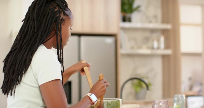 African American friends joining woman tossing salad in bowl at island, plating, tasting meal