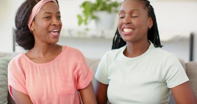 African American mother and daughter exchanging hand squeeze, smiling and sharing memories on sofa