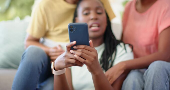 African American family leaning in, teen girl holding blue phone, tapping and sharing clip on couch