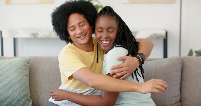 African couple talking, laughing on gray sofa, man reaching shoulder, hugging and showing affection