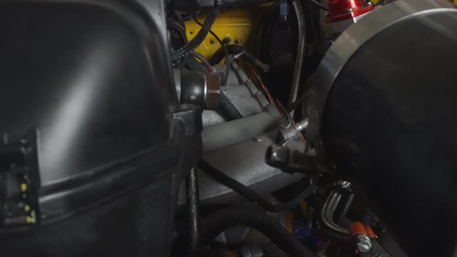Closeup metallic intake pipe and airbox, bright shop lighting, polished aluminum elbow, braided hose couplings, yellow engine block glimpsed, tuning prep atmosphere, boost and horsepower focus,