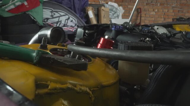 Closeup engine bay with turbo, yellow coolant reservoir, red anodized regulator, braided hoses, metal piping, brick wall backdrop, dim workshop lighting, tuning atmosphere, maintenance scene, tools