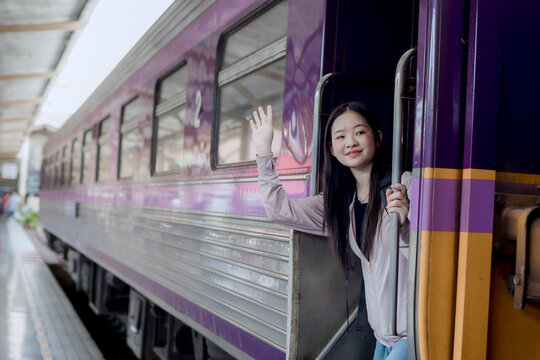 Young Asian woman waving while boarding a train at railway station