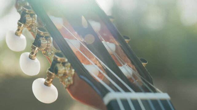 Close-up of the guitar head of a classical guitar with gold pegs. Part of a classical guitar on a blurry background in the park. Head of guitar with nylon strings. Slow motion 4k footage.