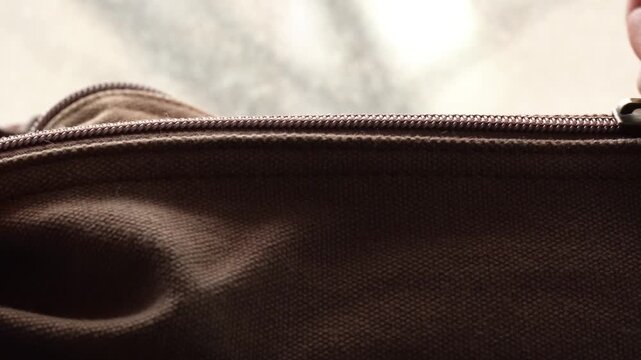 Opening a zip on a brown bag in macro view, zip opening by hand