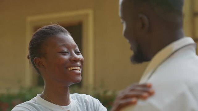 Two lovers exchanging warm gazes and quiet laughter outside their residence. Smiling pair shares tender glances and lighthearted laughter beneath gentle sunlight outside their dwelling