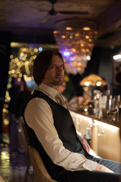 Pensive man in vest sitting at bar counter with bokeh lights, Paris