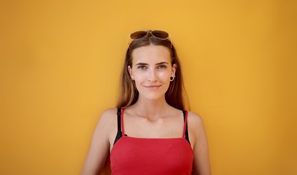 Young woman in a red top smiling against a yellow wall
