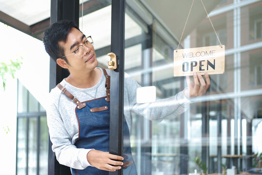 Shop owner hanging open sign on glass storefront door