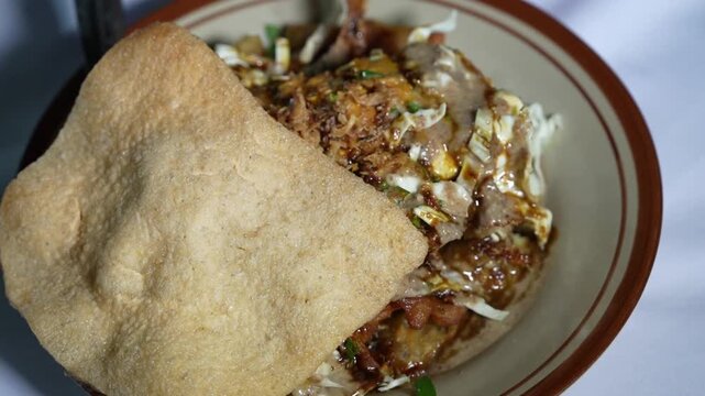 Tahu Gimbal, a specialty of Semarang, Indonesia, with crispy crackers, shredded chicken, bean sprouts, and savory sauce in a close-up view.