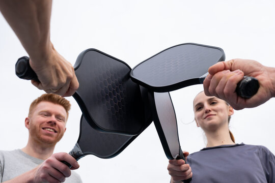 Two friends celebrating a pickleball match, clinking their paddles together