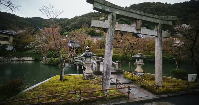 Stone torii gate and bridge in ancient Japanese village with rain falling - steady cam movement