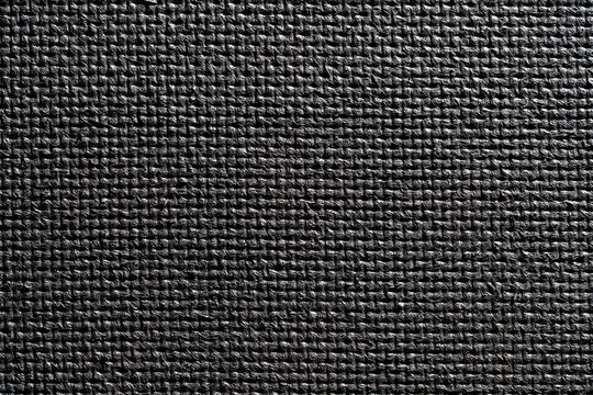Black yoga mat texture background closeup. Full frame macro view of a black rubber fitness mat texture with non slip textured grid pattern