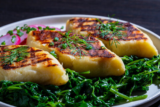 Fried potato dumplings kopytka with spinach and fresh herbs. Closeup of traditional polish kopytka or ukrainian pampushky potato gnocchi served with green spinach and dill on a plate
