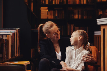 Fototapeta premium Mom and daughter share a joyful moment in a library, surrounded by books. They engage in a meaningful conversation, highlighting the importance of education and personal growth in a warm atmosphere.