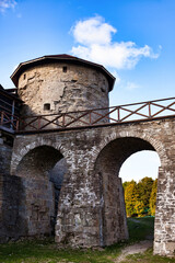 Fototapeta premium A stone archway supports a wooden walkway leading to a round, stone tower. The tower is part of the Koporje fortress on a summer day with blue skies.