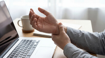 Fototapeta premium Person experiencing wrist pain while working on a laptop computer at a desk