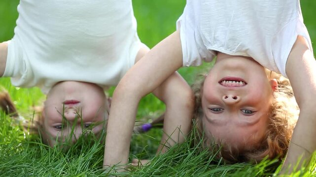 Funny kids do a handstand in a summer park on green grass. Slow motion