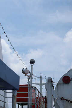 A low-angle vertical commercial photograph showcasing the upper deck superstructure of a marine vessel, featuring mounted outdoor floodlights, a red mechanical pulley wheel