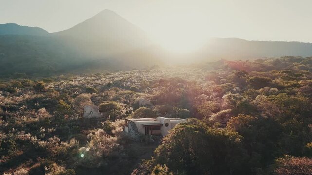 Sunrise Through Forest Trees with Cabins and Volcano Silhouette in Mountain Landscape