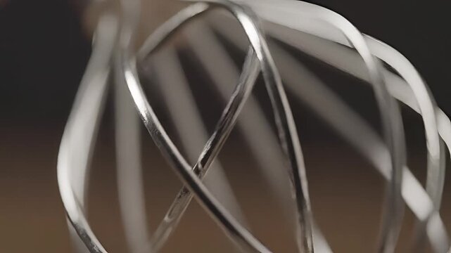 Close up of a metal whisk attachment for a stand mixer spinning.