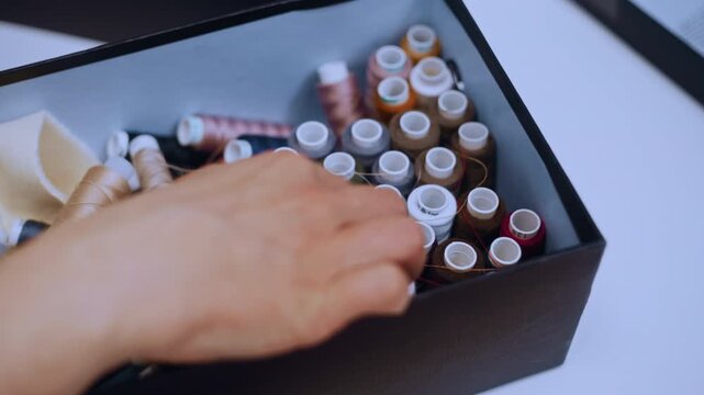 Woman's hands picking a spool of red thread from a box with a colorful assortment for sewing