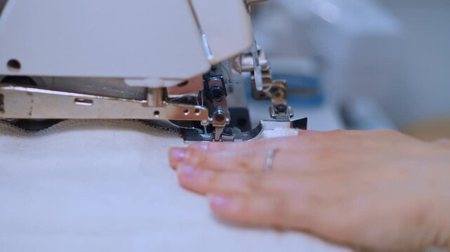 Close-up of a worker's hands sewing white fabric in a textile factory using an overlock machine