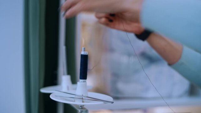 Woman's hands placing a spool of thread on a sewing machine, preparing for needlework