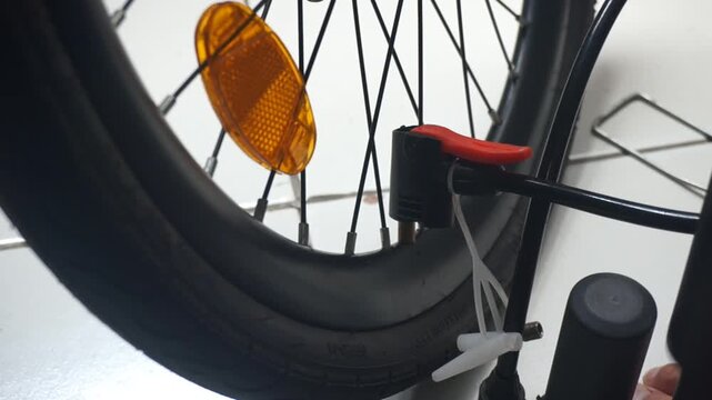 A close-up video of a man's hand using a black hand pump to inflate a flat bicycle tire, demonstrating repair and self-reliance in the outdoors.